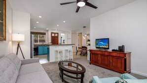 A modern living room with a sofa, a glass coffee table, a TV, and a dining area with chairs and a wooden cabinet.