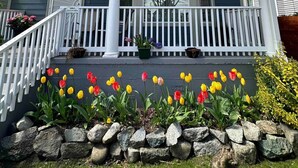 Une maison à deux étages avec un porche, des marches en pierre et une variété de fleurs.