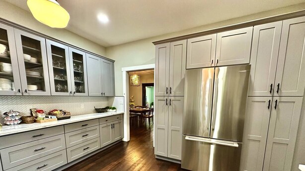 Une cuisine moderne avec des meubles gris, un réfrigérateur en acier inoxydable et un plancher en bois.