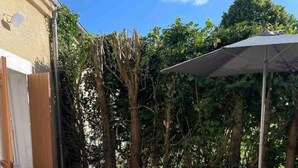 An outdoor patio with a table and chairs, a white umbrella, and a building in the background. - Charmante Maison à la Campagne (Sainte-Fauste)