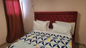 A bedroom with a red headboard, a patterned bedspread, and white pillows.
