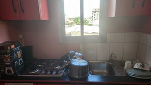 A kitchen with a gas stove, a pot on the stove, a sink, and a window with a view of buildings outside.