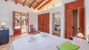 Ein geräumiges Schlafzimmer mit einem großen Bett, einem Holzschrank und Blick auf einen Garten durch eine geöffnete Tür.