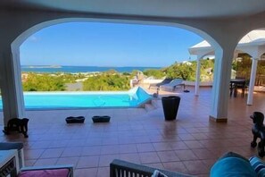 A pool area with a view of the sea, outdoor furniture, and a covered patio.