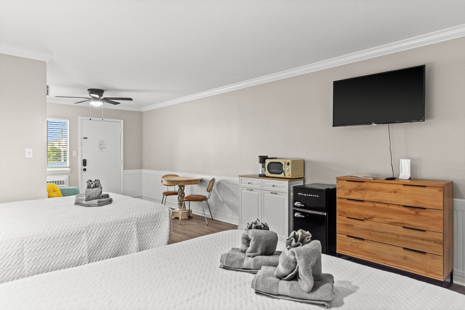 Habitación de hotel con dos camas, una mesa de comedor, microondas, televisor y cómoda de madera.