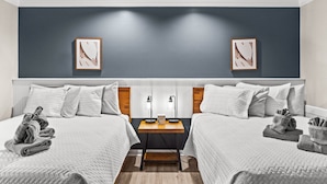 Hotellihuone, jossa on kaksi sänkyä, yöpöytä ja kaksi kehystettyä kuvaa seinällä.