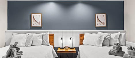 A hotel room with two beds, a nightstand, and two framed pictures on the wall.