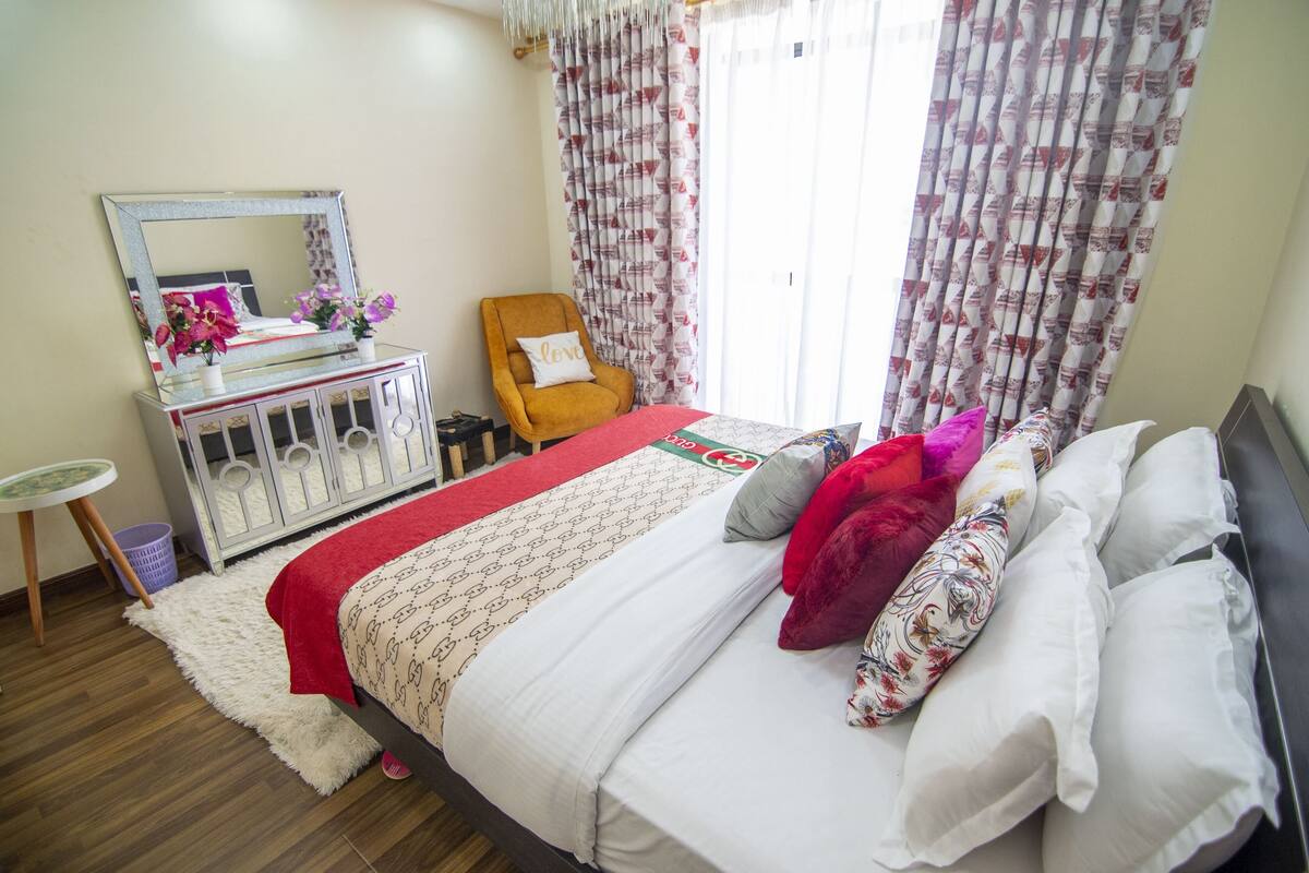 Un dormitorio ordenado con cama, cómoda, silla y espejo.