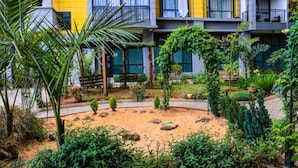 A courtyard with a sandy area, various plants, and a building with balconies. - Lux Suites Silver Habor  Apartments (Nairobi)