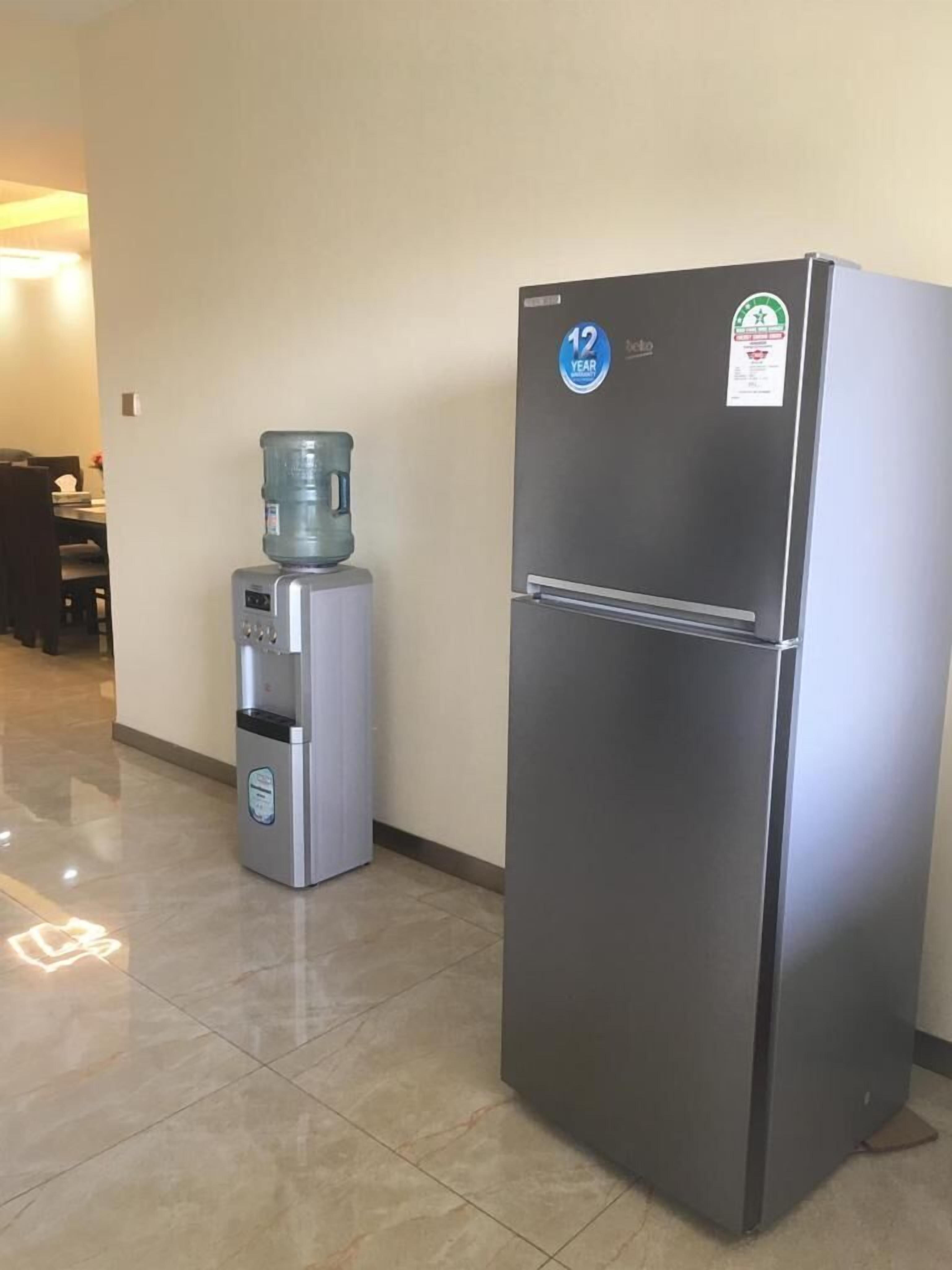 Un refrigerador compacto y un dispensador de agua en un pasillo con piso de baldosas.