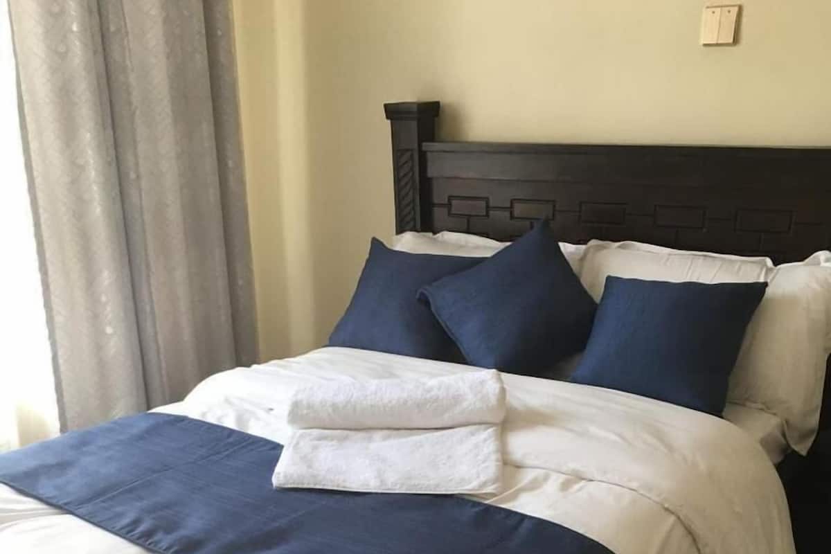 Una cama bien hecha con un cabecero oscuro, ropa de cama blanca y azul marino, y una almohada de acento blanca y esponjosa.
