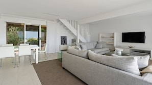 A modern living room with a sofa, TV, and a staircase leading to a balcony.
