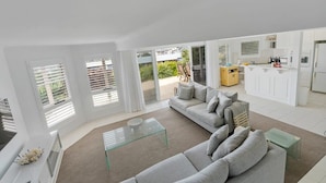 A modern living room with a sofa, glass coffee table, and a view of the kitchen and outdoor area.