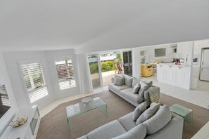 A modern living room with a sofa, glass coffee table, and a view of the kitchen and outdoor area.