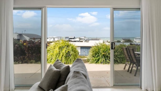 A room with a sliding glass door leading to a balcony with a view of the sea and buildings.