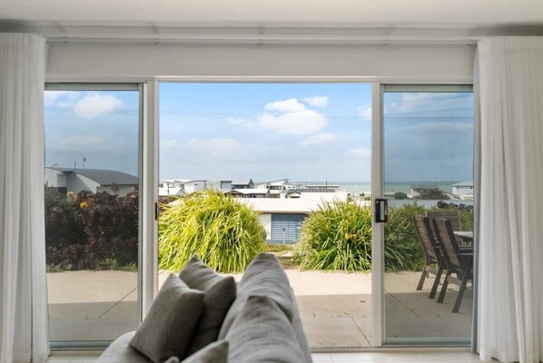 A room with a sliding glass door leading to a balcony with a view of the sea and buildings.