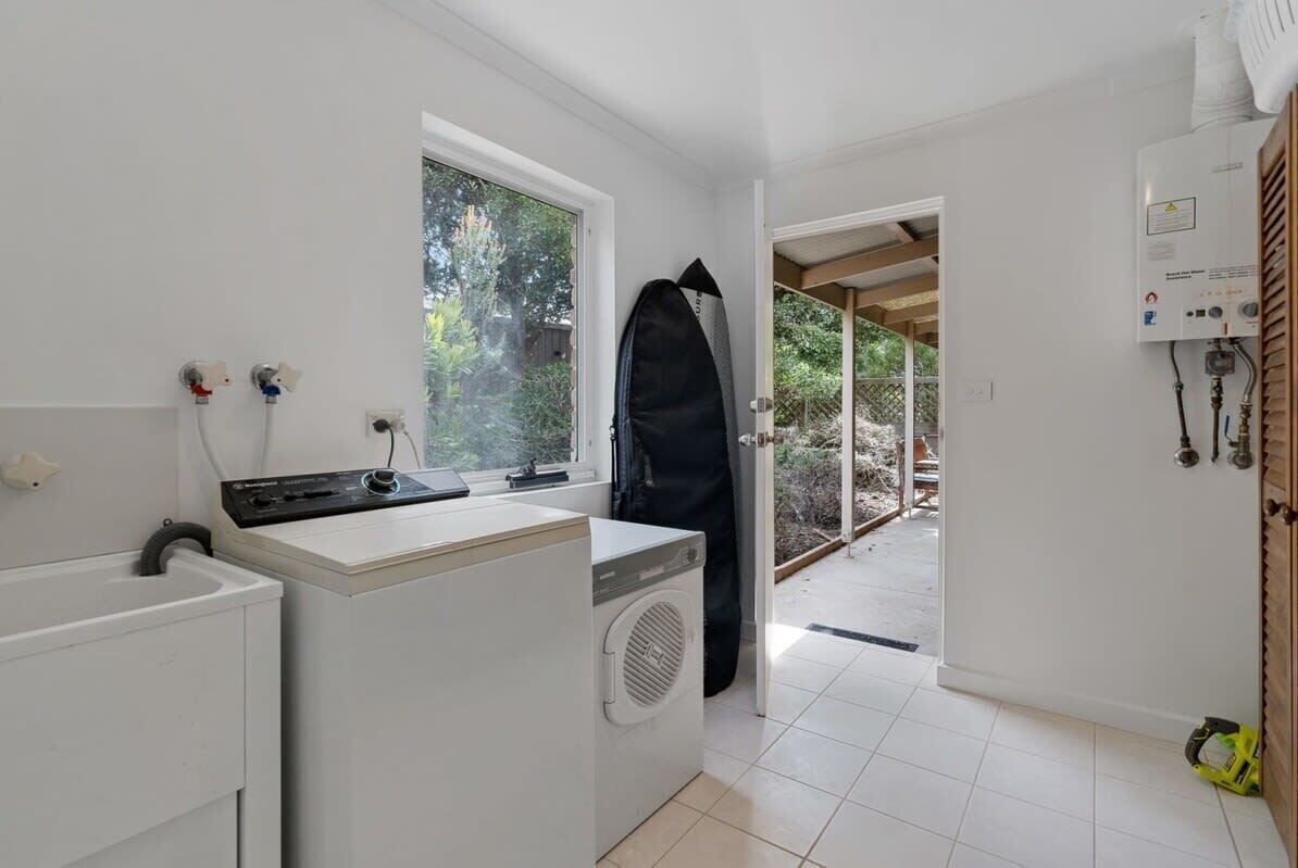 A laundry area with a washing machine, dryer, and a surfboard leaning against the wall.