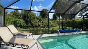 A covered outdoor swimming pool with lounge chairs and a view of tropical vegetation. - Rotonda Heights Pool Home (Rotonda West)