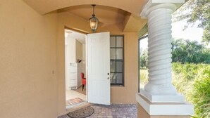 A covered entryway with a brick floor, a white door, and a red chair visible in the background. - This vacation rental home offers a spacious layout  (Rotonda West)