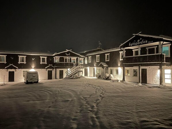 Un patio cubierto de nieve con un edificio que dice 'Hyttgarden Husd' y un vehículo cubierto.