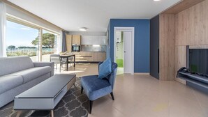 A modern living room with a sofa, a coffee table, and a TV stand. There is a kitchen in the background with a dining area. - Sea View Studio Superior (Umag)