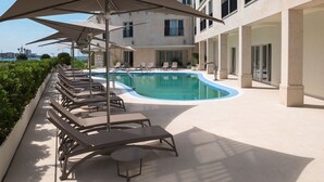 A poolside area with lounge chairs and umbrellas, a swimming pool, and a building with multiple windows and balconies. - Sea View Studio Superior (Umag)