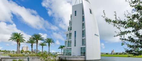 Un bâtiment moderne doté d’un toit incurvé original, entouré d’un plan d’eau et de palmiers.