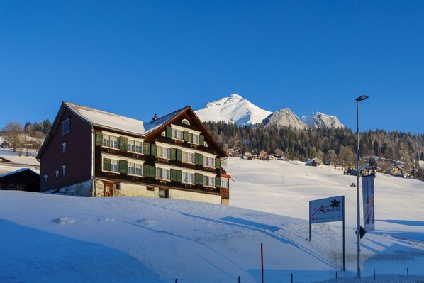 A traditional chalet-style building with a snow-covered roof, situated in a mountainous area with a clear sky. - Hotel Toggenburg (Wildhaus-Alt St. Johann)
