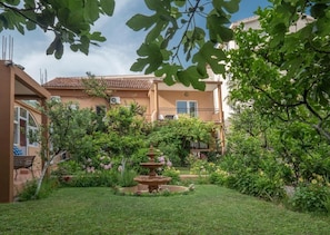 A courtyard with a fountain, lush greenery, and a building with a tiled roof.