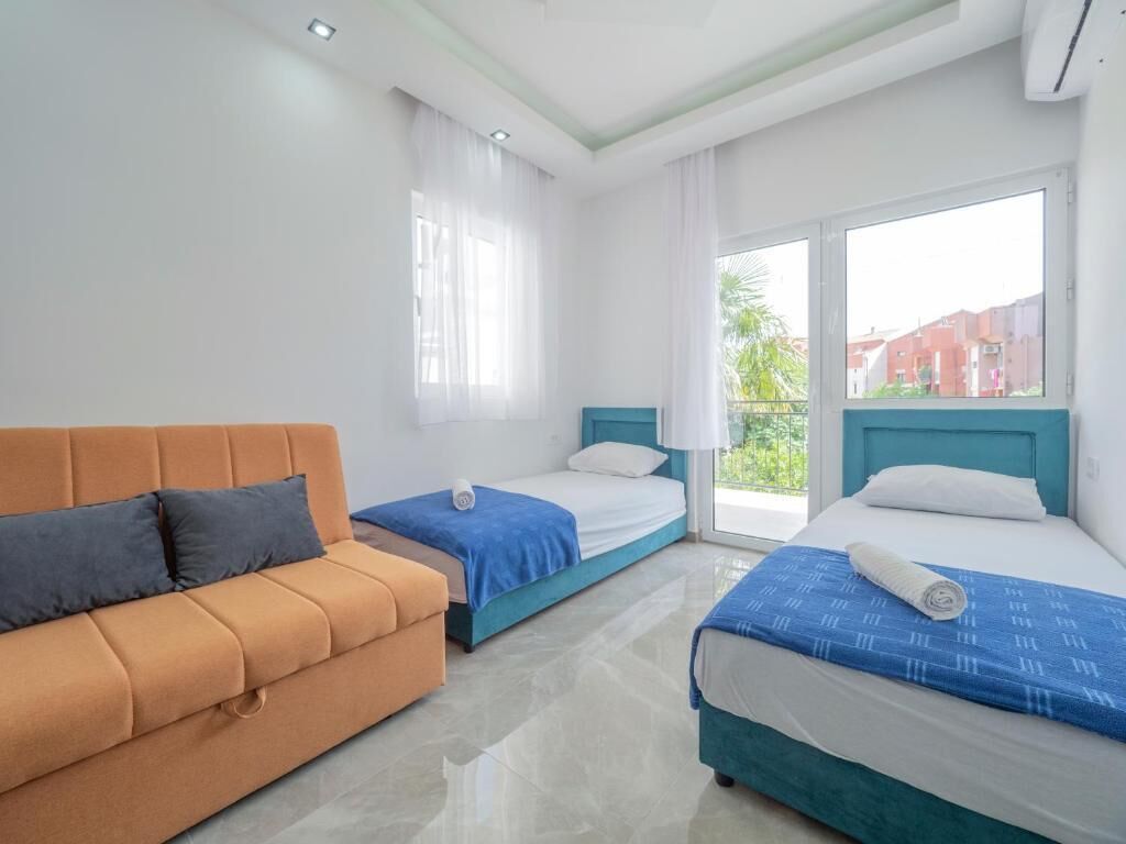 Habitación de hotel con dos camas, un sofá y ventanas amplias.