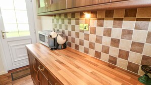 Una cucina con pensili in legno, un forno a microonde, un bollitore e uno schienale piastrellato.