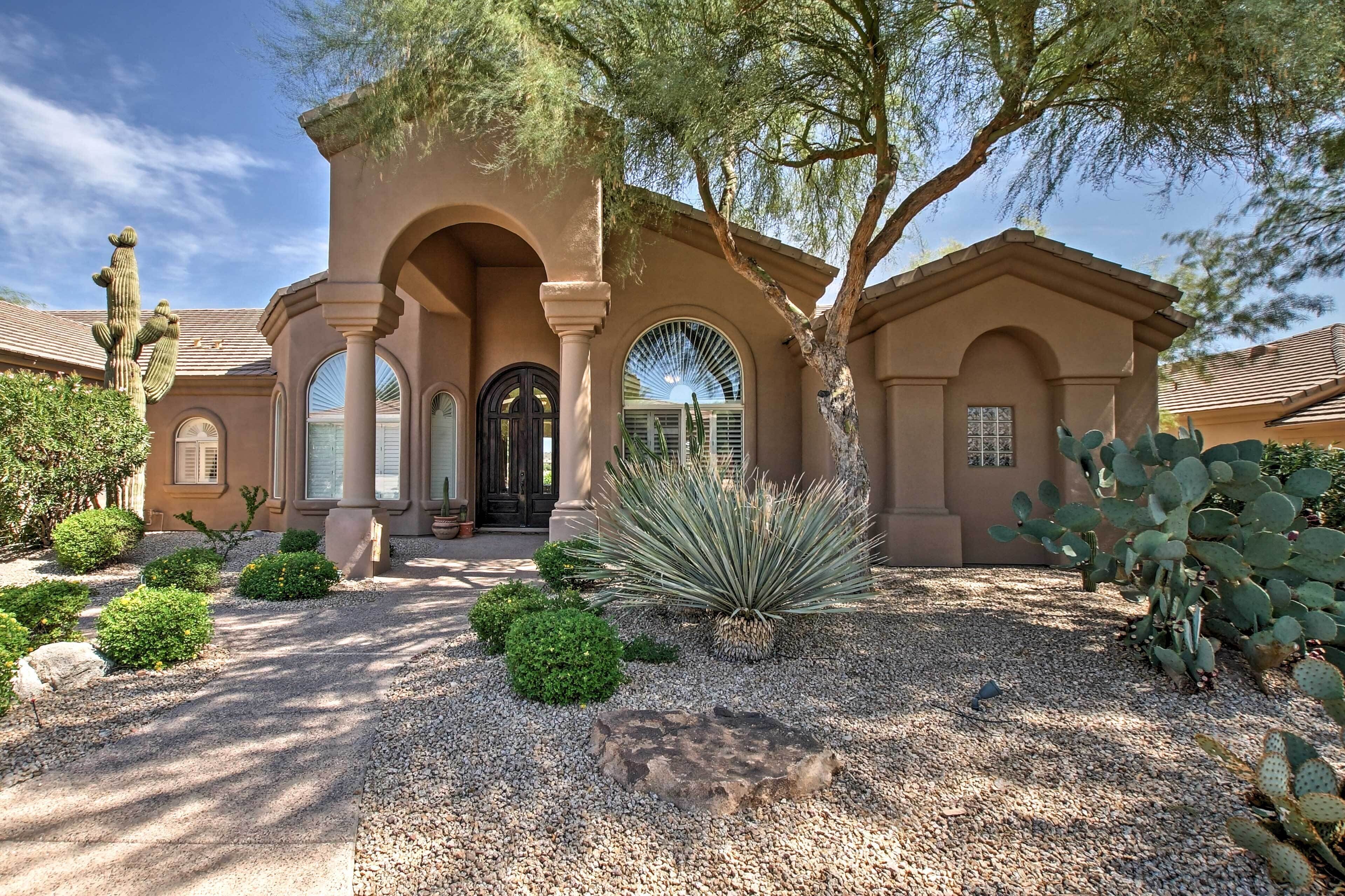 A house with a stucco exterior, arched doorways, and a gravel driveway.
