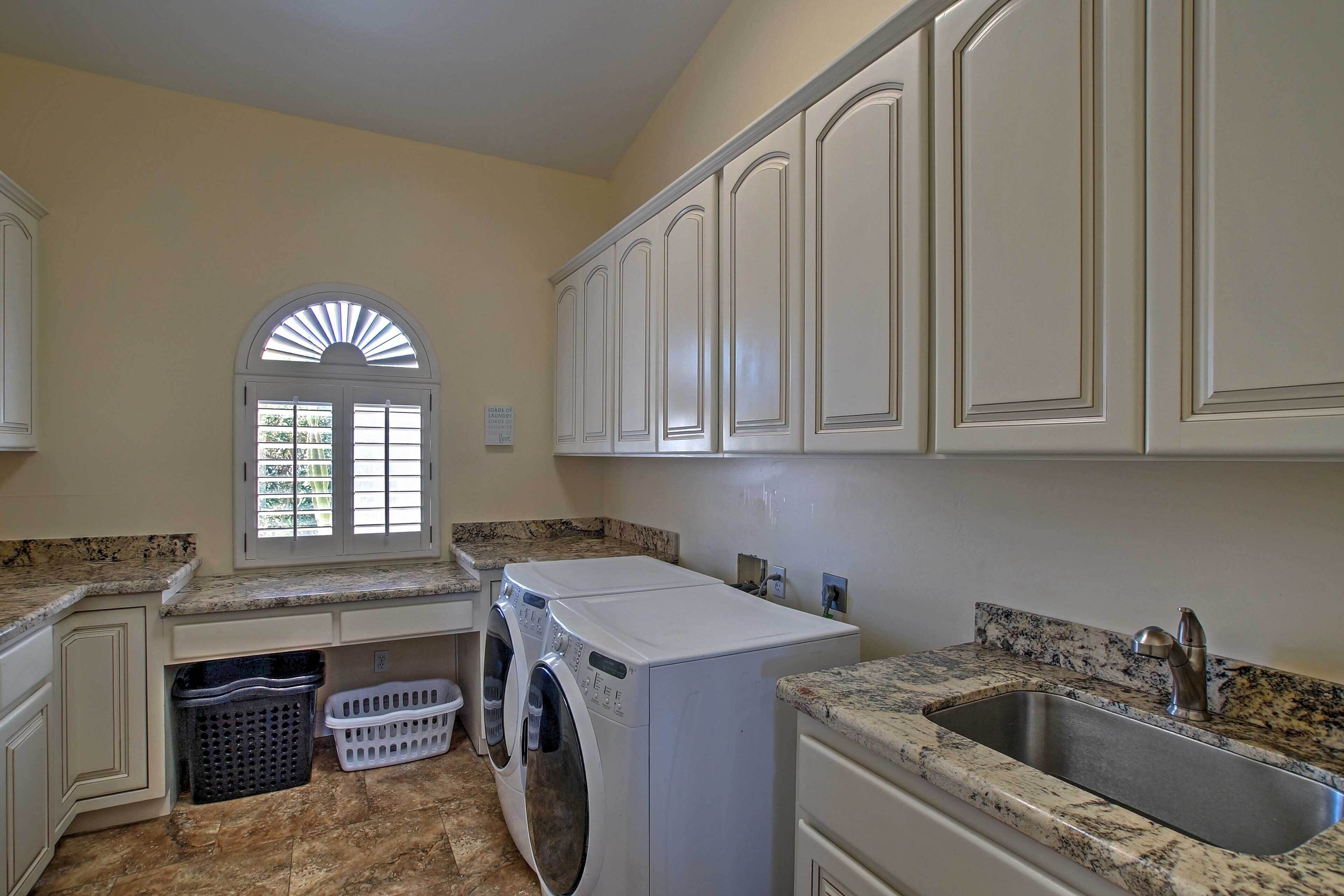 A laundry room with a washing machine, a sink, and a window with blinds.