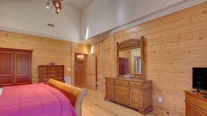 A room with wooden paneling, a bed with a pink blanket, a dresser, a mirror, and a television.