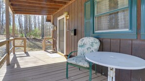 Une terrasse en bois avec une table et une chaise, une boîte aux lettres et une fenêtre avec des volets.