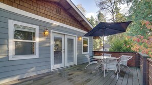 Une terrasse en bois avec une table et des chaises, un espace couvert avec un parasol, et une maison avec une fenêtre et une porte.