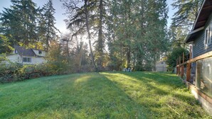 Une cour arrière verdoyante avec une maison, entourée de grands arbres et dotée d’une terrasse en bois.