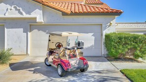 Une voiturette de golf rouge est garée devant une maison dont le portail de garage est blanc et dont le toit est recouvert de tuiles rouges.