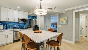 A modern kitchen with white cabinets, a marble countertop, and a built-in microwave. There is a dining area with a table and chairs. - Upscale Naples Condo w/ Pool Access: Walk to Pier! (Naples)
