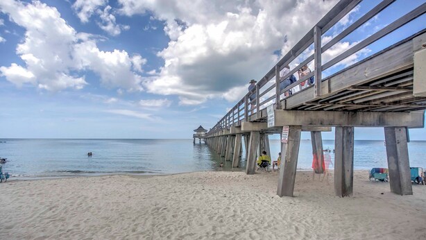 A beach with a wooden pier extending into the water, a sandy beach, and a clear sky with clouds. - Upscale Naples Condo w/ Pool Access: Walk to Pier! (Naples)