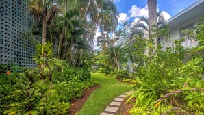 A lush garden with a stone pathway leading to a grassy area, surrounded by various tropical plants and a lattice fence. - Upscale Naples Condo w/ Pool Access: Walk to Pier! (Naples)