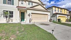 Kaksikerroksinen talo, jossa on autotalli, etupiha ja kirkas taivas.