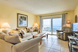 A living room with a sofa set, a coffee table, and a chair. There is a large window with curtains and a view of the outside. - Oceanfront Cocoa Beach Condo w/ View: Walk to Pier (Cocoa Beach)