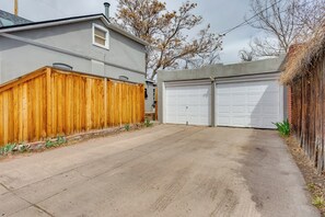 Un garage con una porta bianca, un recinto in legno e un vialetto in cemento.