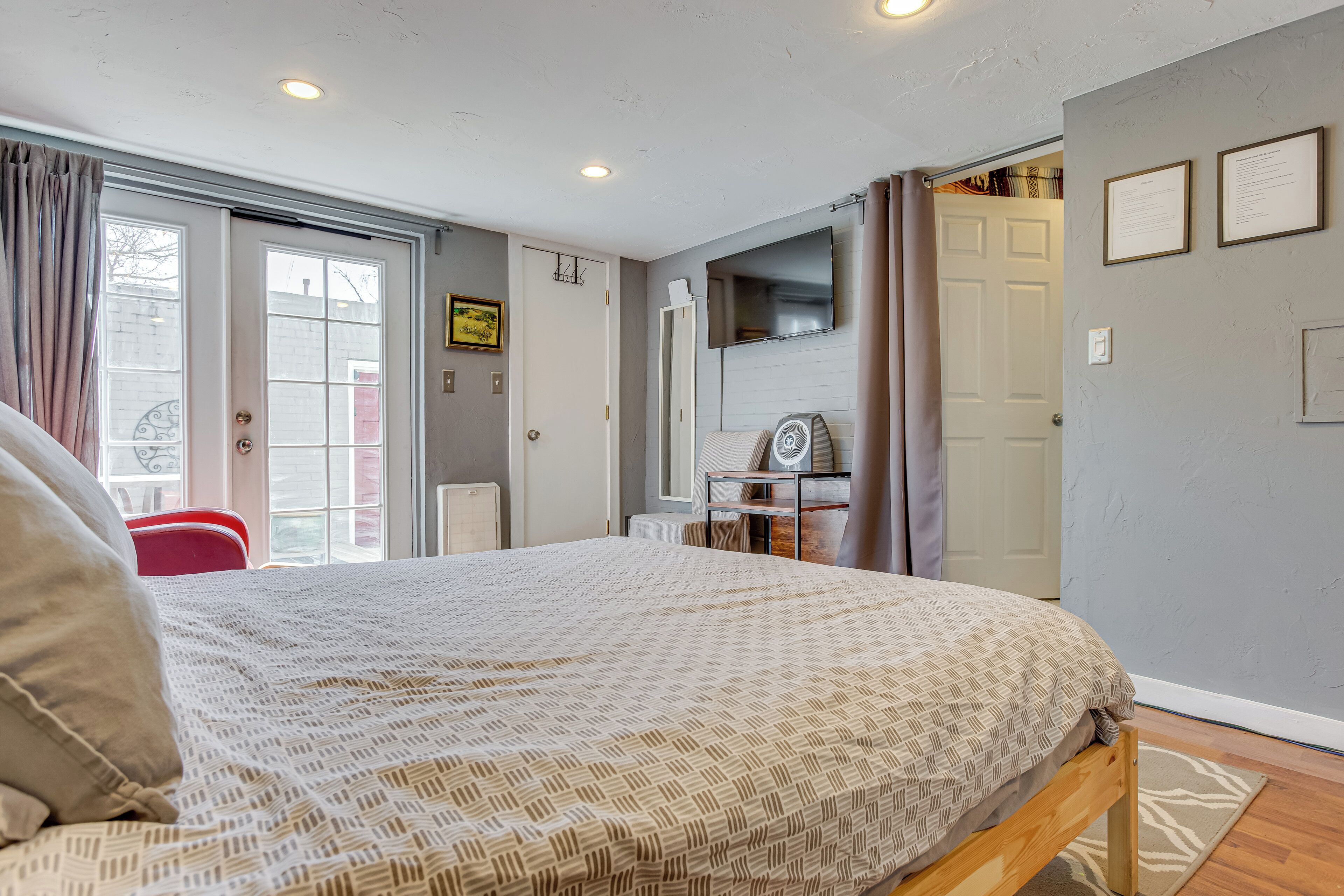 A bedroom with a bed, a desk, a chair, a TV, and a door leading to another room.