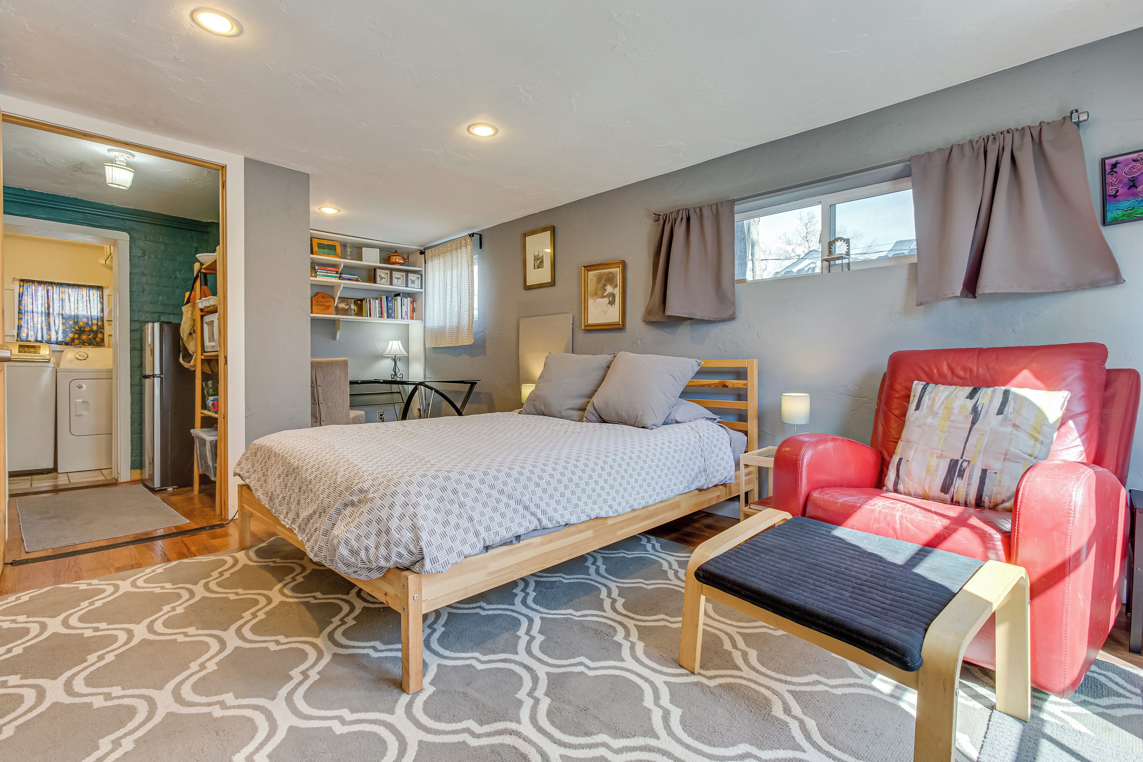 A bedroom with a bed, a red chair, a wooden bench, a desk, and a bookshelf.