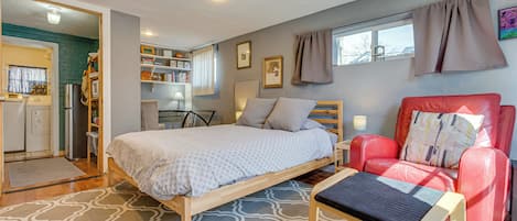 Un dormitorio con una cama, una silla roja, un banco de madera, un escritorio y una estantería.