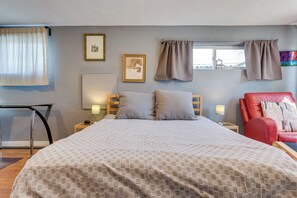 A neatly arranged bedroom with a large bed, two bedside tables, a red chair, and a window with curtains.