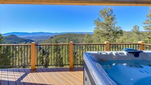 Een houten terras met een jacuzzi en uitzicht op bergen en bossen.