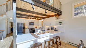 Een moderne keuken met een groot eiland, houten balken en uitzicht op de omgeving.